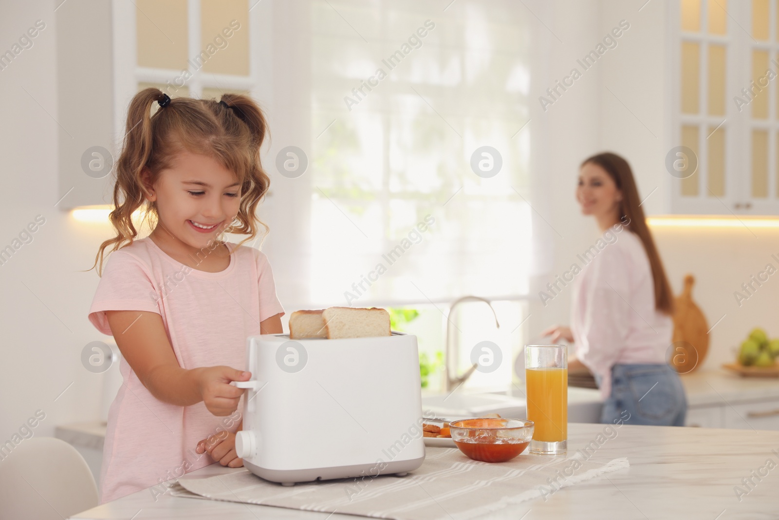 Cute little girl using toaster at table in kitchen Photo of Cute little girl using toaster at table in kitchen