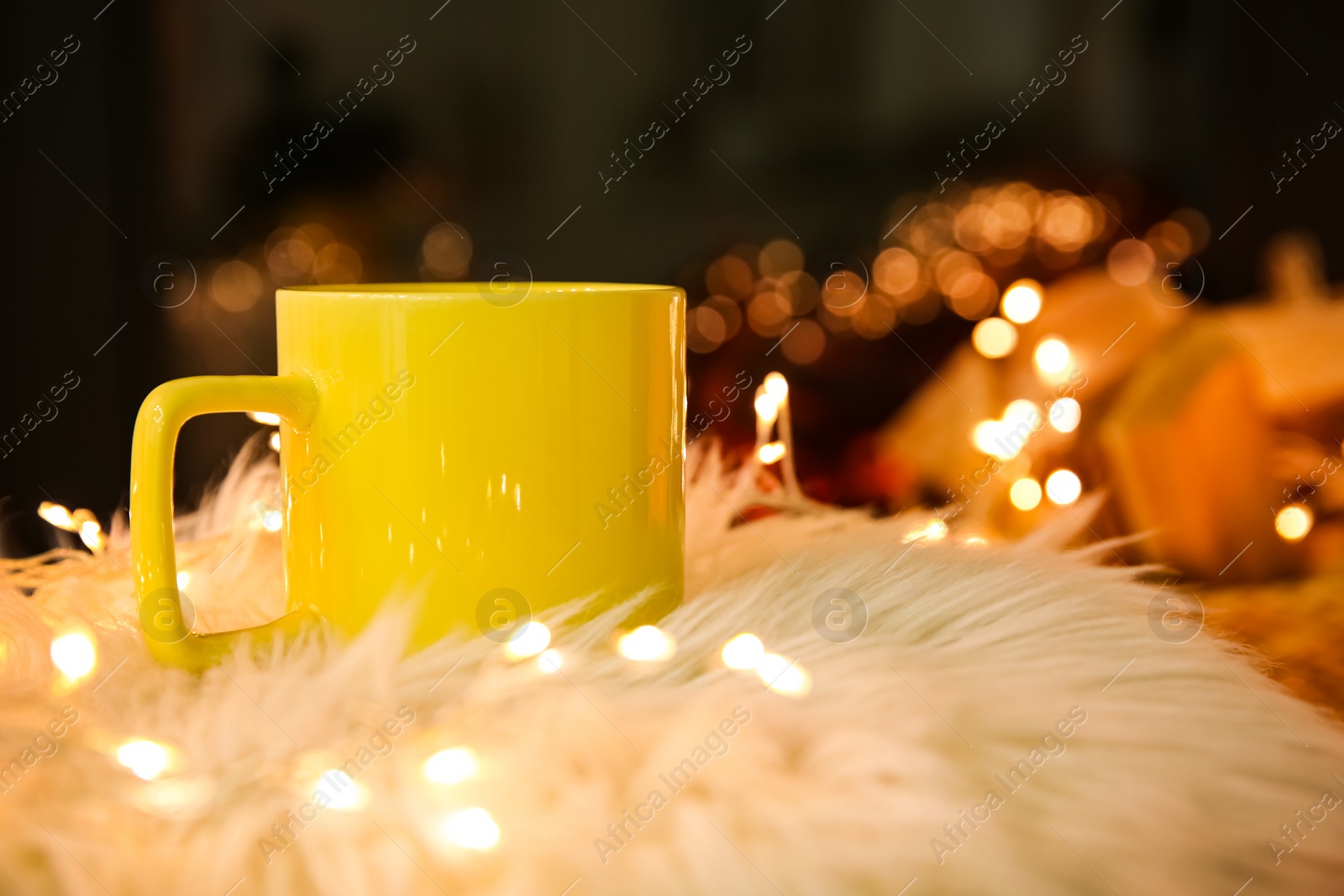 Yellow cup with hot drink and fairy lights on faux fur Photo of Yellow cup with hot drink and fairy lights on faux fur