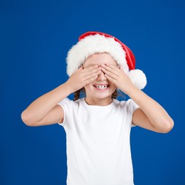 Happy little child in Santa hat closing eyes on blue background. Christmas celebration Image of Happy little child in Santa hat closing eyes on blue background. Christmas celebration