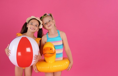 Cute little children in beachwear with bright inflatable toys on pink background. Space for text Photo of Cute little children in beachwear with bright inflatable toys on pink background. Space for text