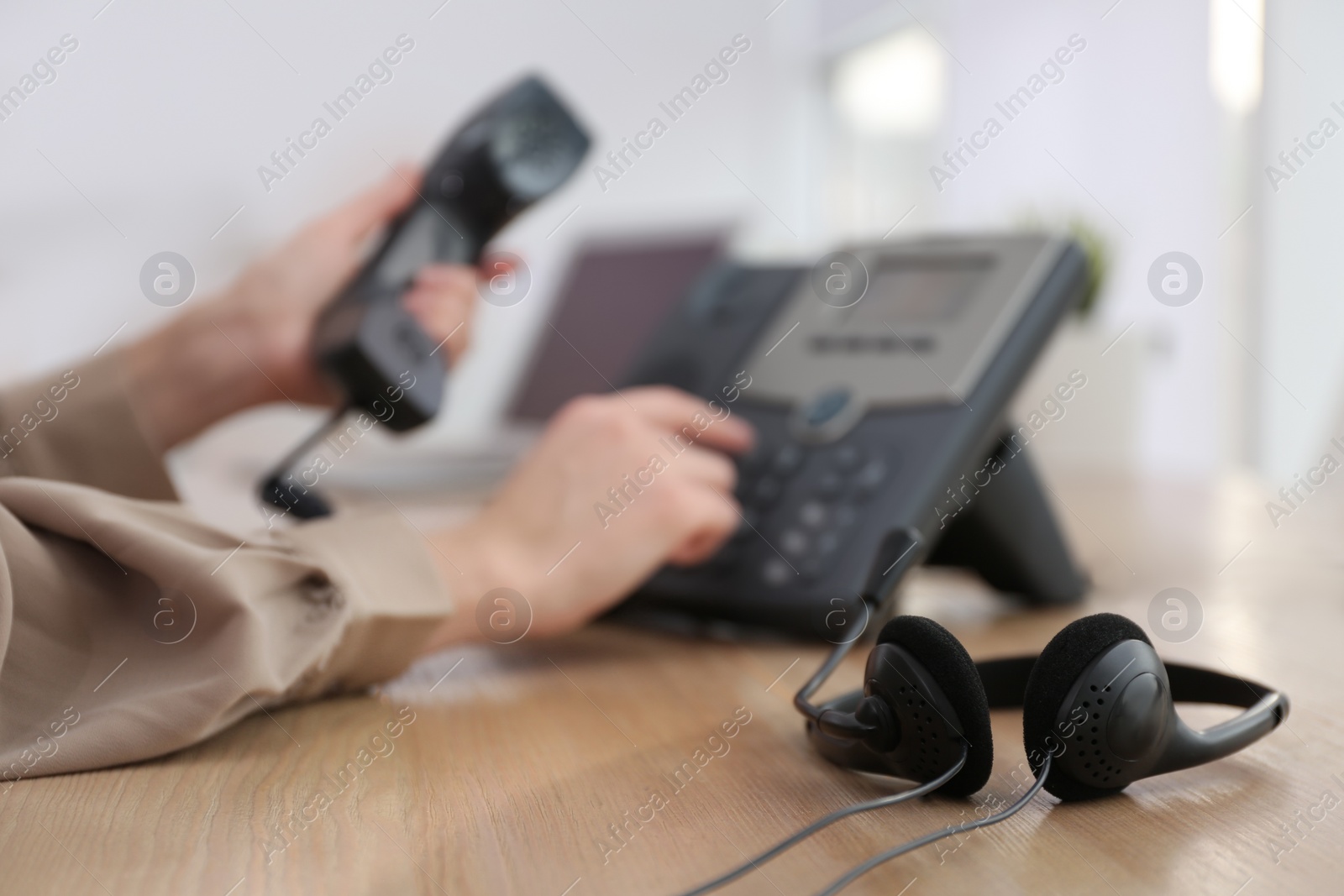Woman using desktop telephone in office, focus on headset. Hotline service Photo of Woman using desktop telephone in office, focus on headset. Hotline service