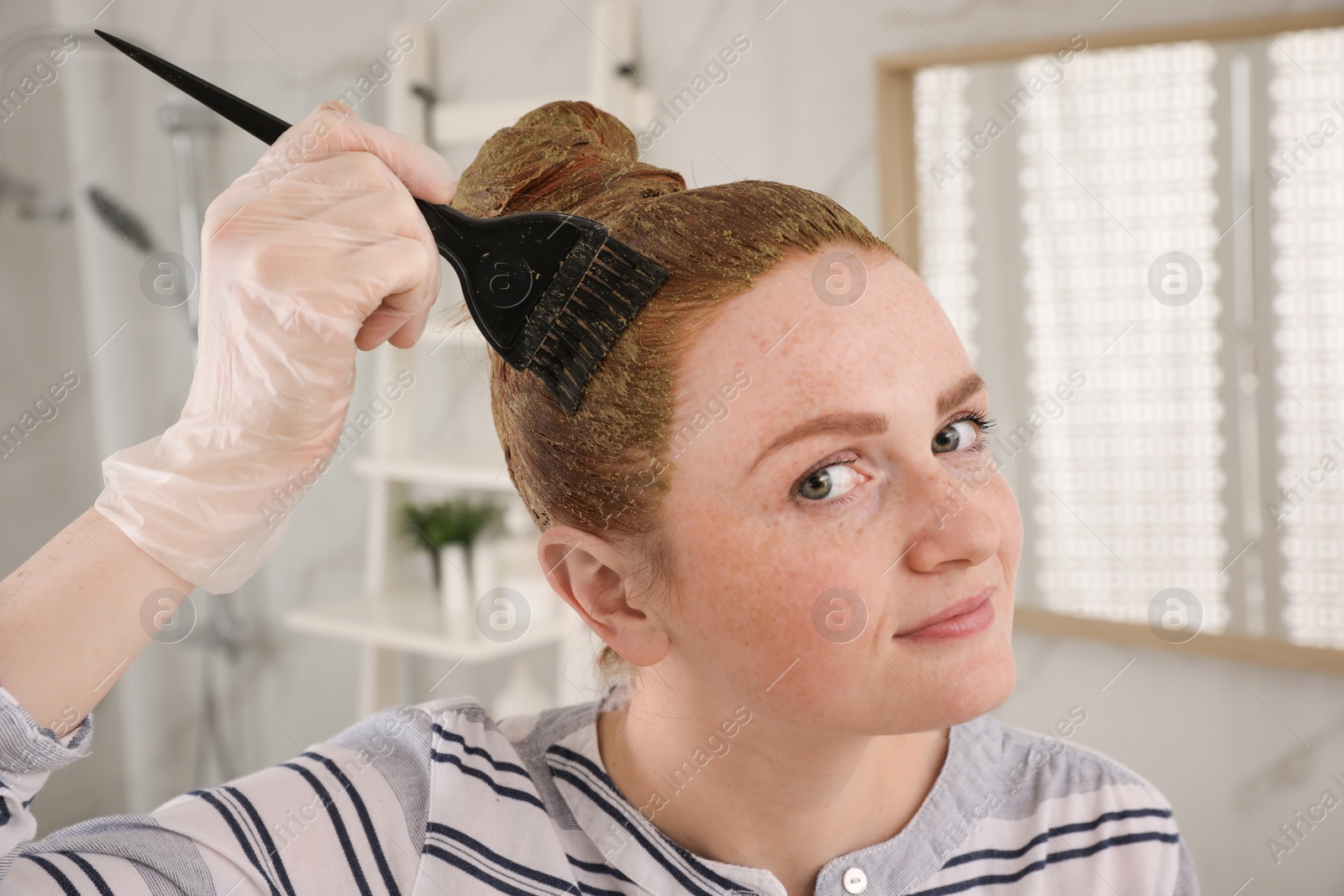 Young woman dyeing her hair with henna in bathroom Photo of Young woman dyeing her hair with henna in bathroom