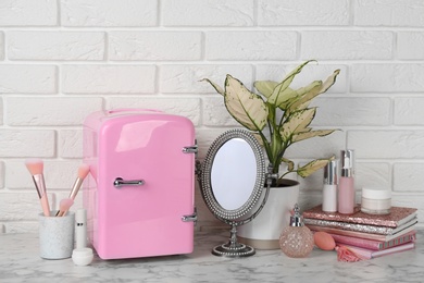 Cosmetic refrigerator and skin care products on white marble table Photo of Cosmetic refrigerator and skin care products on white marble table