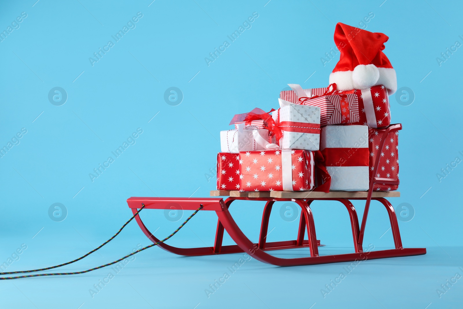 Sleigh with gift boxes and Santa hat on light blue background. Space for text Photo of Sleigh with gift boxes and Santa hat on light blue background. Space for text