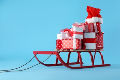 Sleigh with gift boxes and Santa hat on light blue background. Space for text Photo of Sleigh with gift boxes and Santa hat on light blue background. Space for text