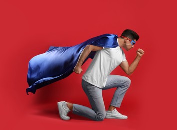 Man wearing superhero cape and mask on red background Photo of Man wearing superhero cape and mask on red background