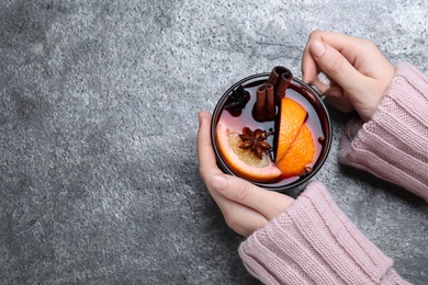 Woman with glass cup of mulled wine at grey table, top view. Space for text Photo of Woman with glass cup of mulled wine at grey table, top view. Space for text