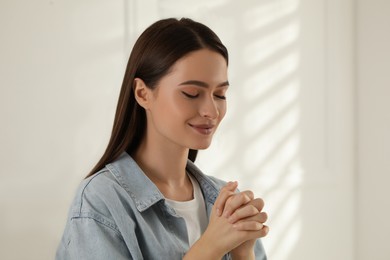 Religious young woman with clasped hands praying indoors Photo of Religious young woman with clasped hands praying indoors