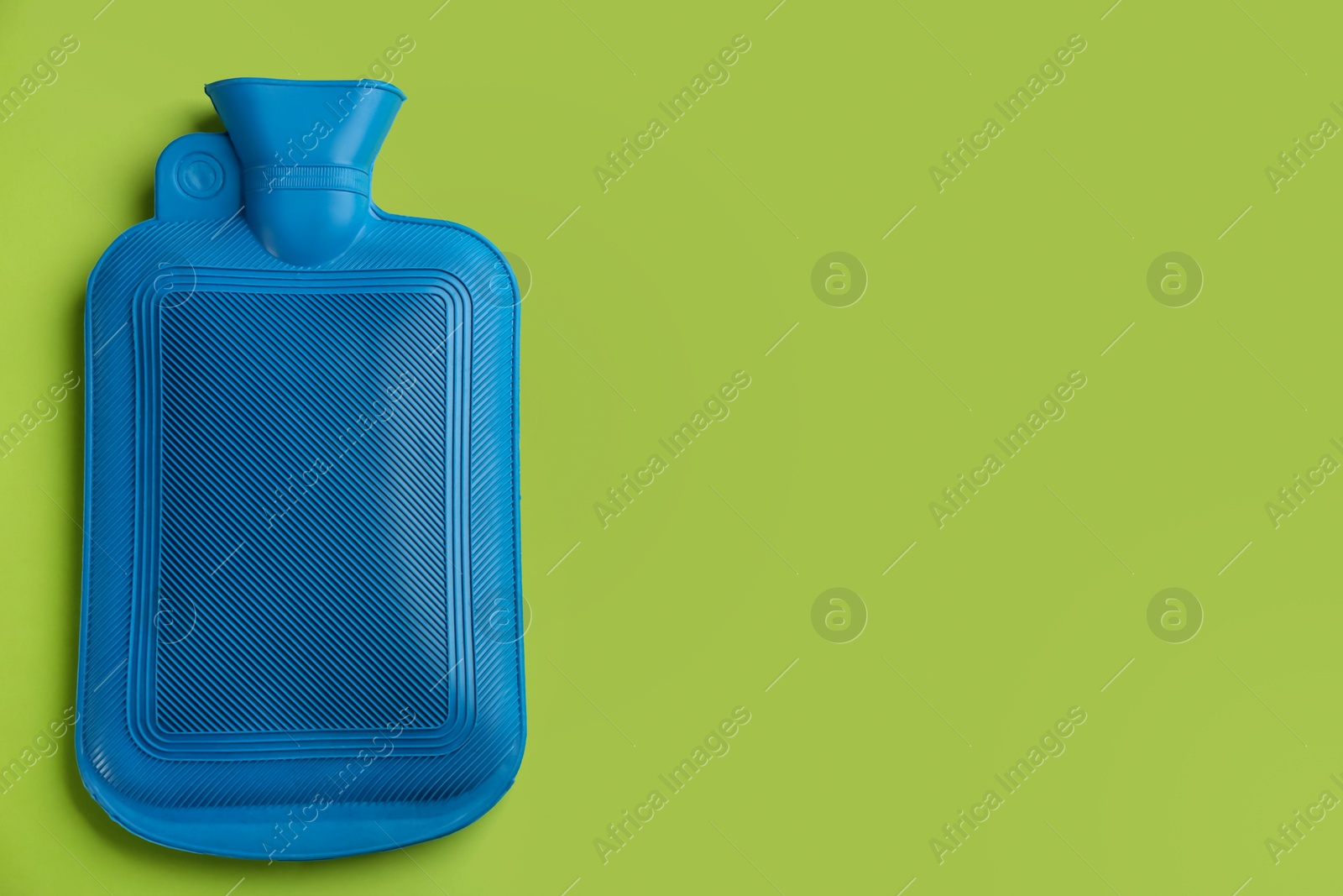 Photo of Blue rubber hot water bottle on green background, top view. Space for text