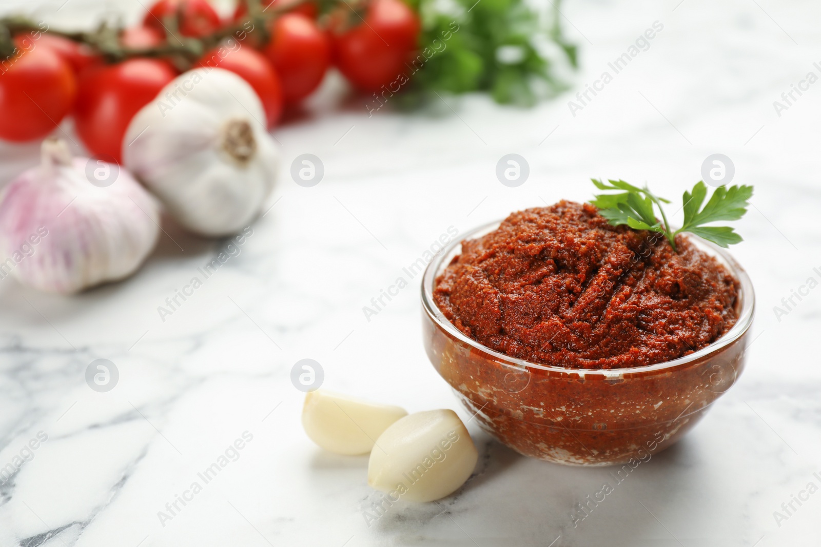 Delicious adjika sauce in glass bowl and ingredients on white marble table, closeup Photo of Delicious adjika sauce in glass bowl and ingredients on white marble table, closeup