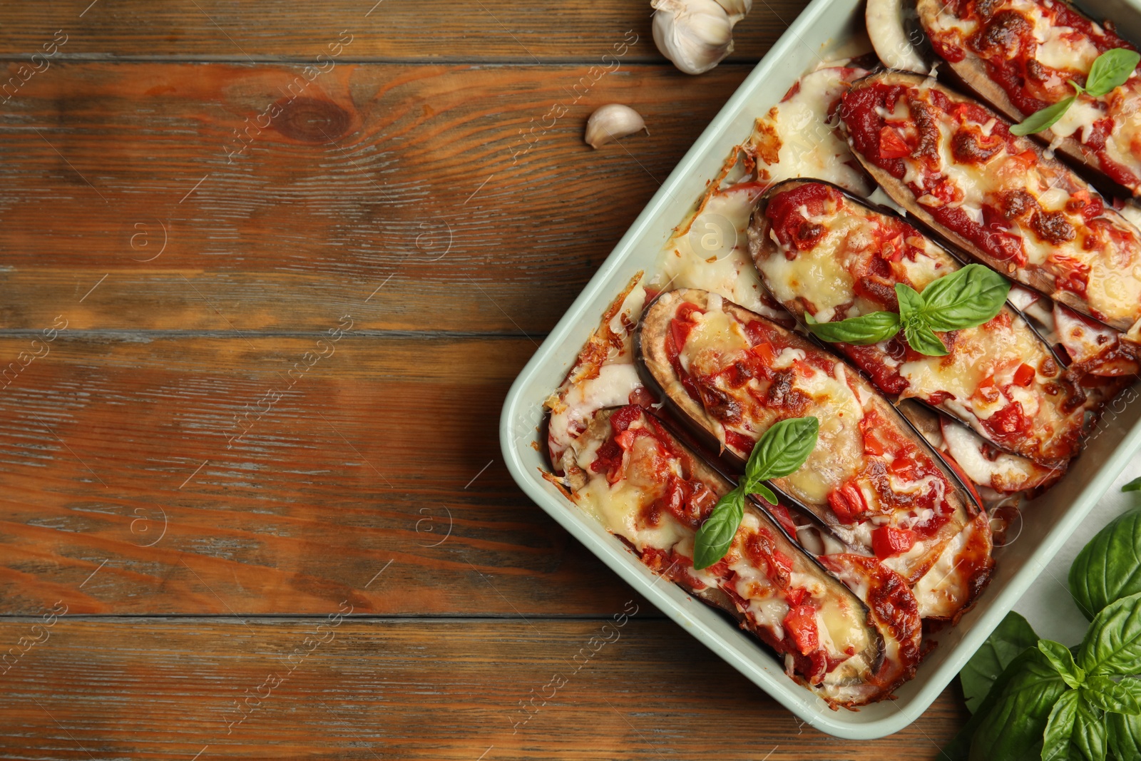 Baked eggplant with tomatoes, cheese and basil in dishware on wooden table, flat lay. Space for text Photo of Baked eggplant with tomatoes, cheese and basil in dishware on wooden table, flat lay. Space for text
