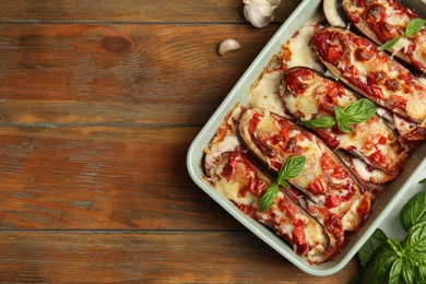 Baked eggplant with tomatoes, cheese and basil in dishware on wooden table, flat lay. Space for text Photo of Baked eggplant with tomatoes, cheese and basil in dishware on wooden table, flat lay. Space for text