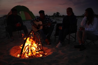 Group of friends gathering around bonfire on beach in evening. Camping season Photo of Group of friends gathering around bonfire on beach in evening. Camping season
