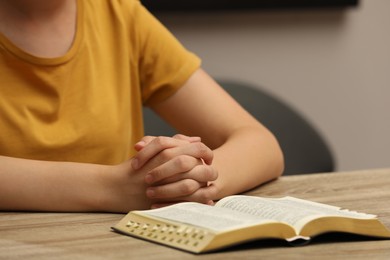 Religious woman praying over Bible at wooden table indoors, closeup Photo of Religious woman praying over Bible at wooden table indoors, closeup