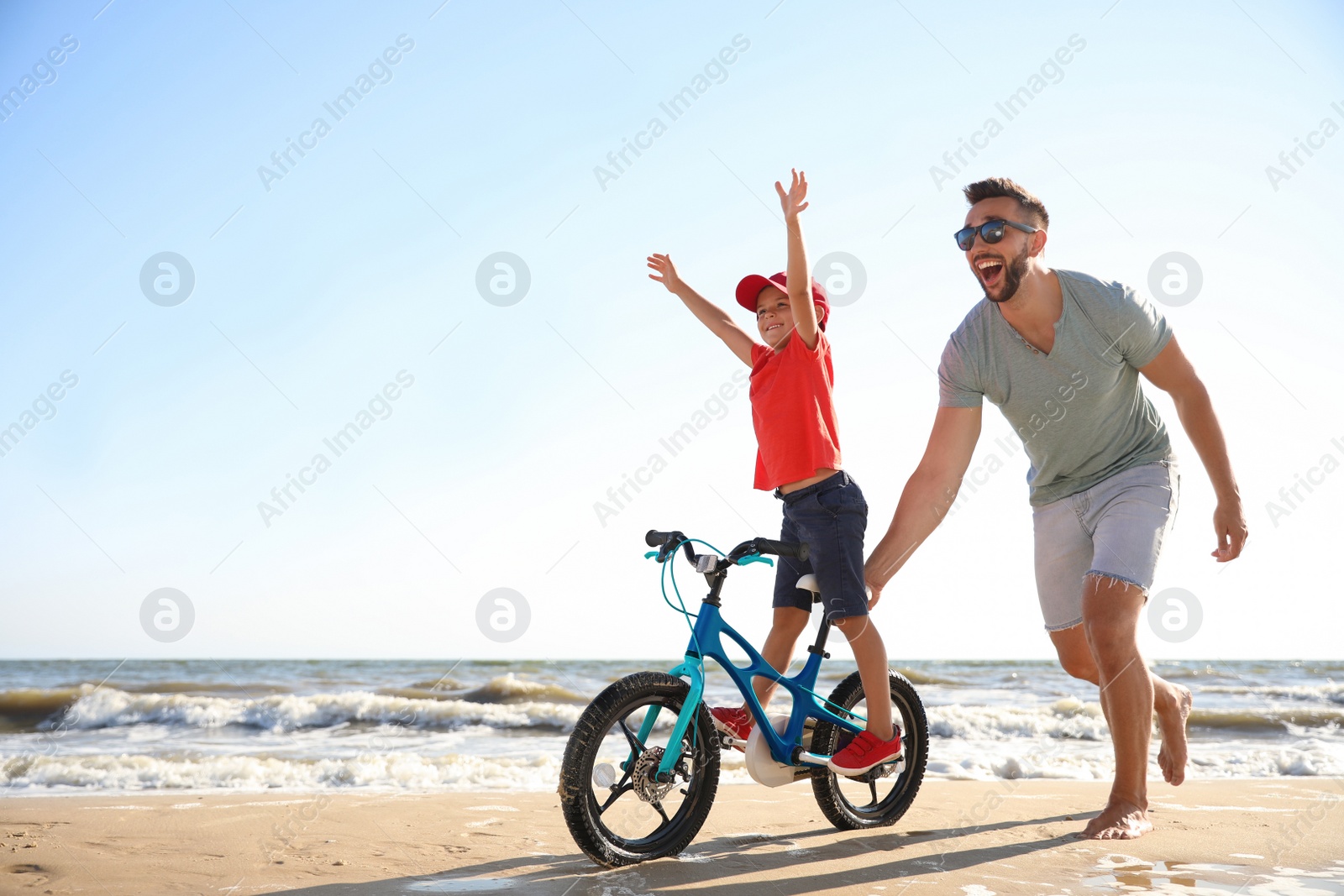 Photo of Happy father teaching son to ride bicycle on sandy beach near sea