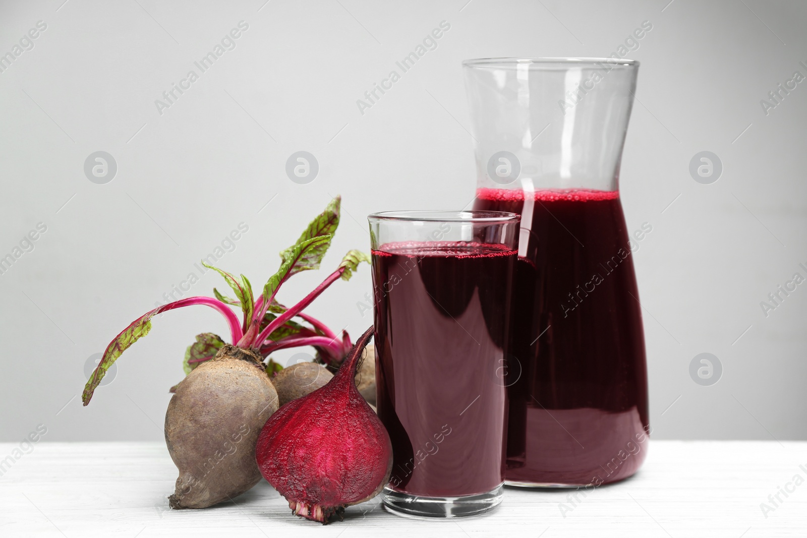 Fresh beet juice and raw vegetable on white wooden table Photo of Fresh beet juice and raw vegetable on white wooden table