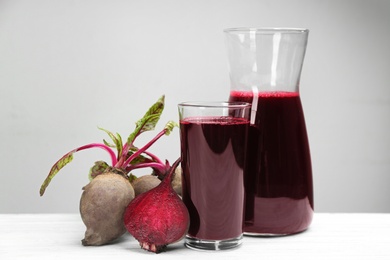 Fresh beet juice and raw vegetable on white wooden table Photo of Fresh beet juice and raw vegetable on white wooden table