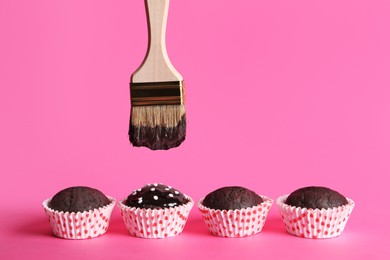 Spreading glaze onto chocolate muffins with brush on pink background Photo of Spreading glaze onto chocolate muffins with brush on pink background