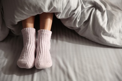 Woman wearing knitted socks under blanket in bed, closeup Photo of Woman wearing knitted socks under blanket in bed, closeup