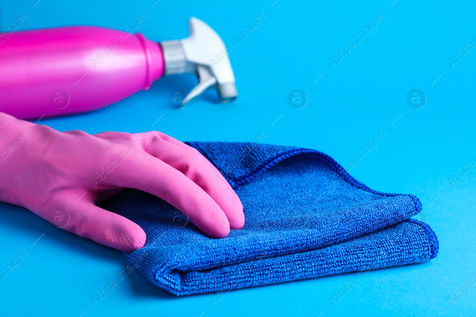 Woman in pink rubber gloves with microfiber cloth and detergent on light blue background, closeup Photo of Woman in pink rubber gloves with microfiber cloth and detergent on light blue background, closeup