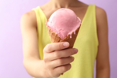 Woman holding pink ice cream in wafer cone on violet background, closeup Photo of Woman holding pink ice cream in wafer cone on violet background, closeup