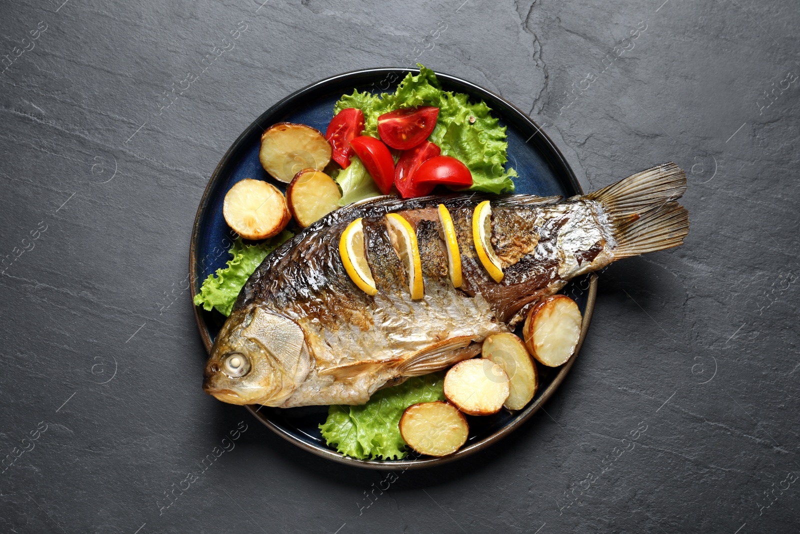 Tasty homemade roasted crucian carp with garnish on black table, top view. River fish Photo of Tasty homemade roasted crucian carp with garnish on black table, top view. River fish