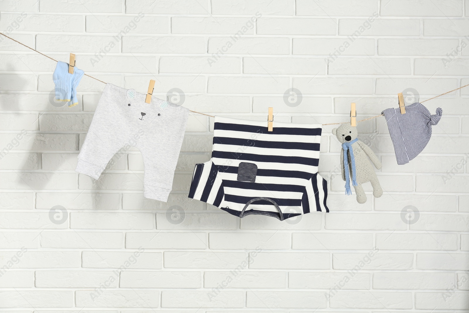 Baby clothes hanging on washing line near white brick wall Photo of Baby clothes hanging on washing line near white brick wall