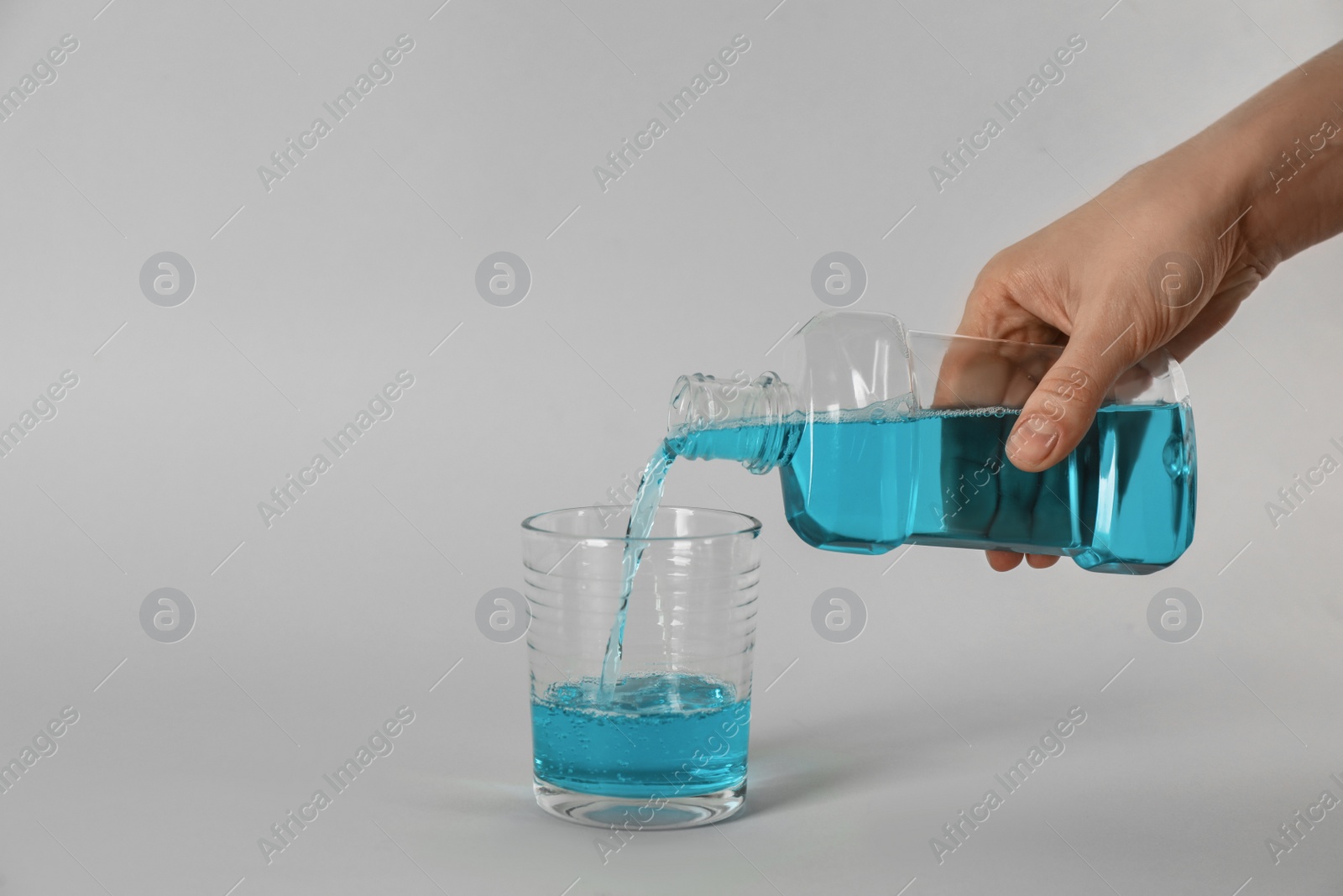 Woman pouring mouthwash into glass on light grey background, closeup Photo of Woman pouring mouthwash into glass on light grey background, closeup