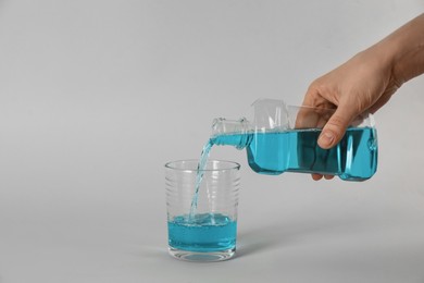 Woman pouring mouthwash into glass on light grey background, closeup Photo of Woman pouring mouthwash into glass on light grey background, closeup