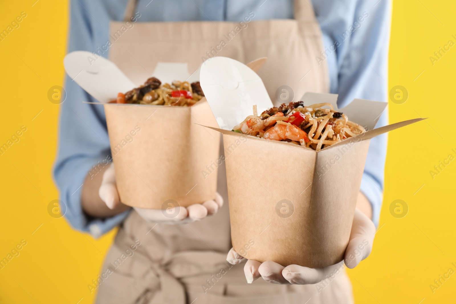 Chef holding boxes of wok noodles with seafood on yellow background, closeup Photo of Chef holding boxes of wok noodles with seafood on yellow background, closeup