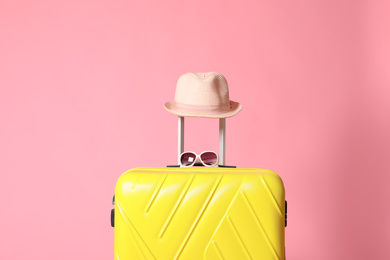 Photo of Yellow suitcase with sunglasses and hat on pink background