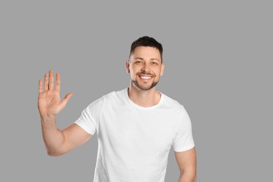 Cheerful man waving to say hello on light grey background Photo of Cheerful man waving to say hello on light grey background