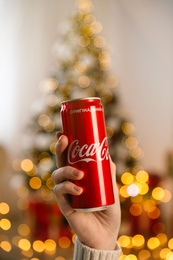 MYKOLAIV, UKRAINE - January 01, 2021: Woman with can of Coca-Cola against blurred Christmas tree indoors, closeup Photo of MYKOLAIV, UKRAINE - January 01, 2021: Woman with can of Coca-Cola against blurred Christmas tree indoors, closeup