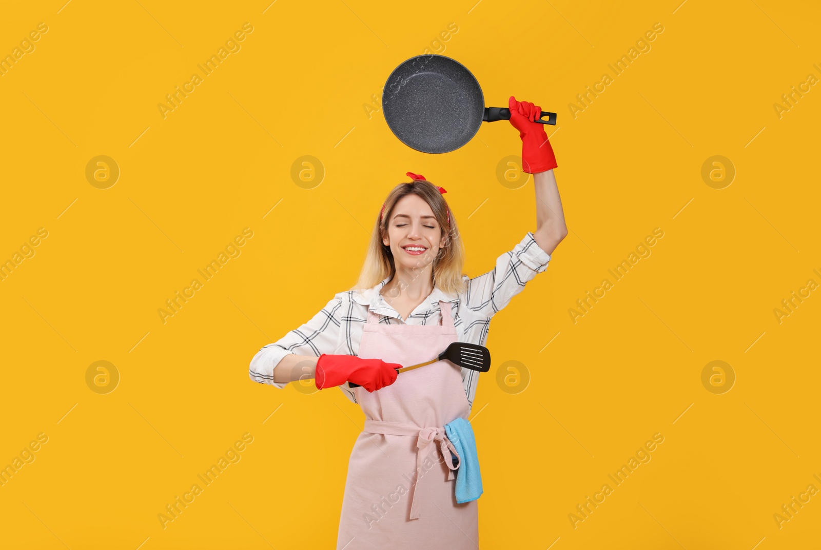 Young housewife meditating with frying pan and spatula on yellow background Photo of Young housewife meditating with frying pan and spatula on yellow background