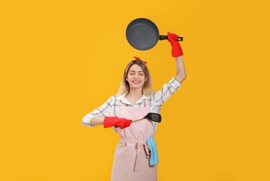 Young housewife meditating with frying pan and spatula on yellow background Photo of Young housewife meditating with frying pan and spatula on yellow background