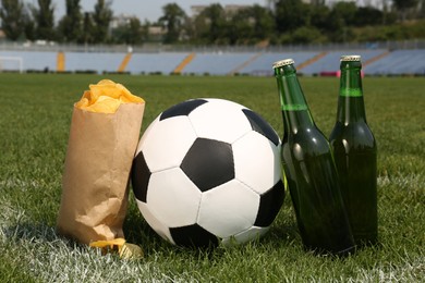 Football ball with beer and chips on green field grass in stadium Photo of Football ball with beer and chips on green field grass in stadium