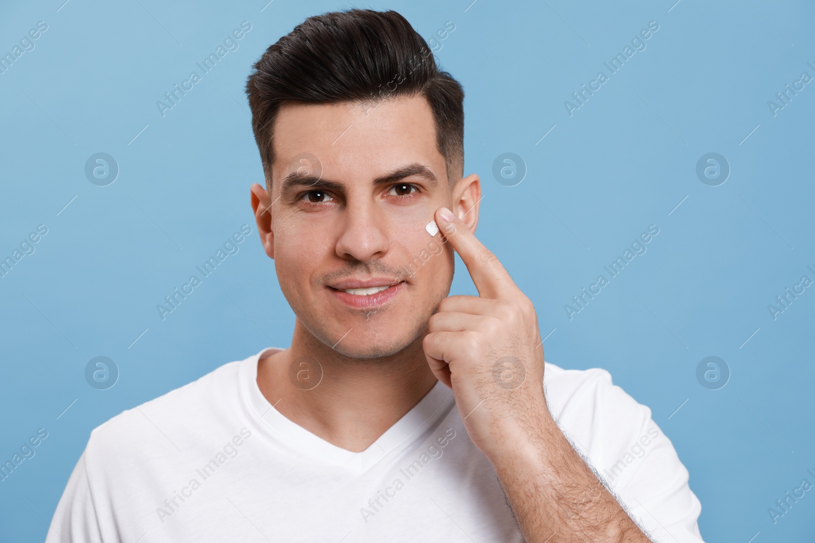 Happy handsome man applying face cream against turquoise background Photo of Happy handsome man applying face cream against turquoise background