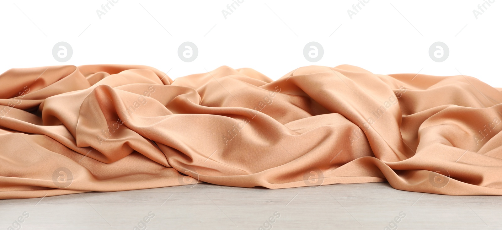 Photo of Beautiful peach silk on wooden table against white background