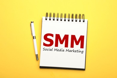 Notebook with text SMM (Social media marketing) and pen on yellow background, flat lay Image of Notebook with text SMM (Social media marketing) and pen on yellow background, flat lay