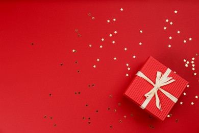 Gift box and shiny confetti on red background, top view. Space for text Photo of Gift box and shiny confetti on red background, top view. Space for text