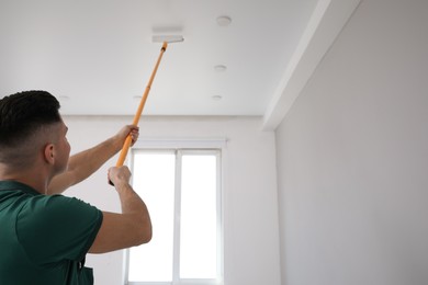 Man painting ceiling with roller in room. Space for text Photo of Man painting ceiling with roller in room. Space for text