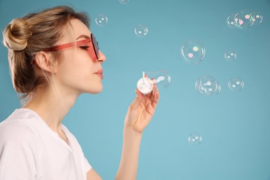 Young woman blowing soap bubbles on light blue background, space for text Photo of Young woman blowing soap bubbles on light blue background, space for text