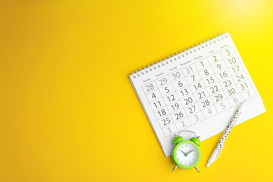 Calendar, pen and alarm clock on yellow background, flat lay. Space for text Image of Calendar, pen and alarm clock on yellow background, flat lay. Space for text