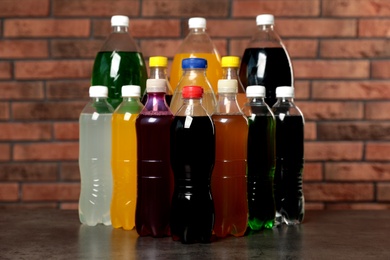 Bottles of soft drinks on table near brick wall Photo of Bottles of soft drinks on table near brick wall