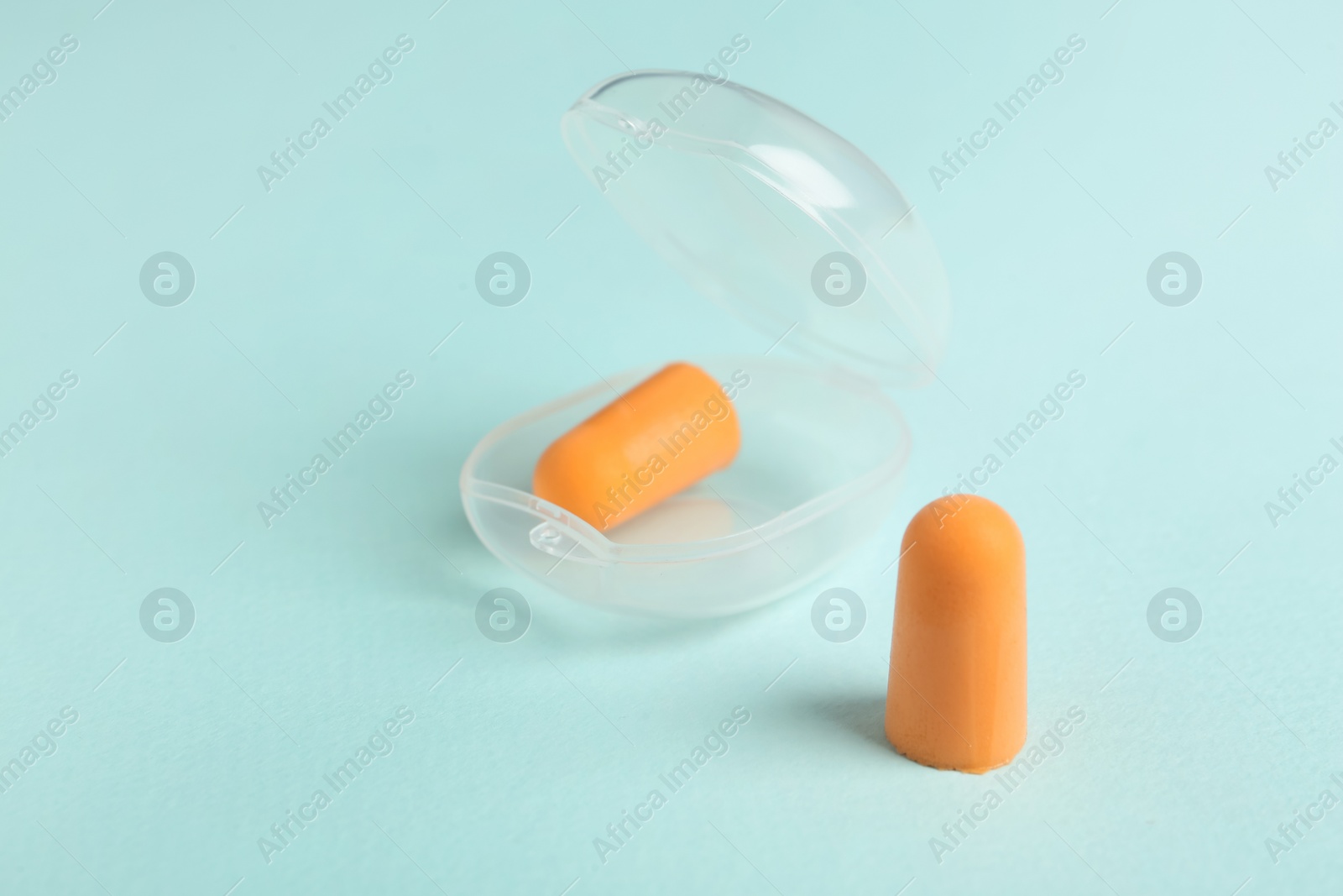 Pair of orange ear plugs and case on turquoise background Photo of Pair of orange ear plugs and case on turquoise background