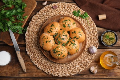 Traditional pampushka buns with garlic and herbs on wooden table, flat lay Photo of Traditional pampushka buns with garlic and herbs on wooden table, flat lay