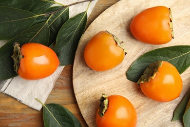 Delicious fresh persimmons and green leaves on wooden table, flat lay Photo of Delicious fresh persimmons and green leaves on wooden table, flat lay