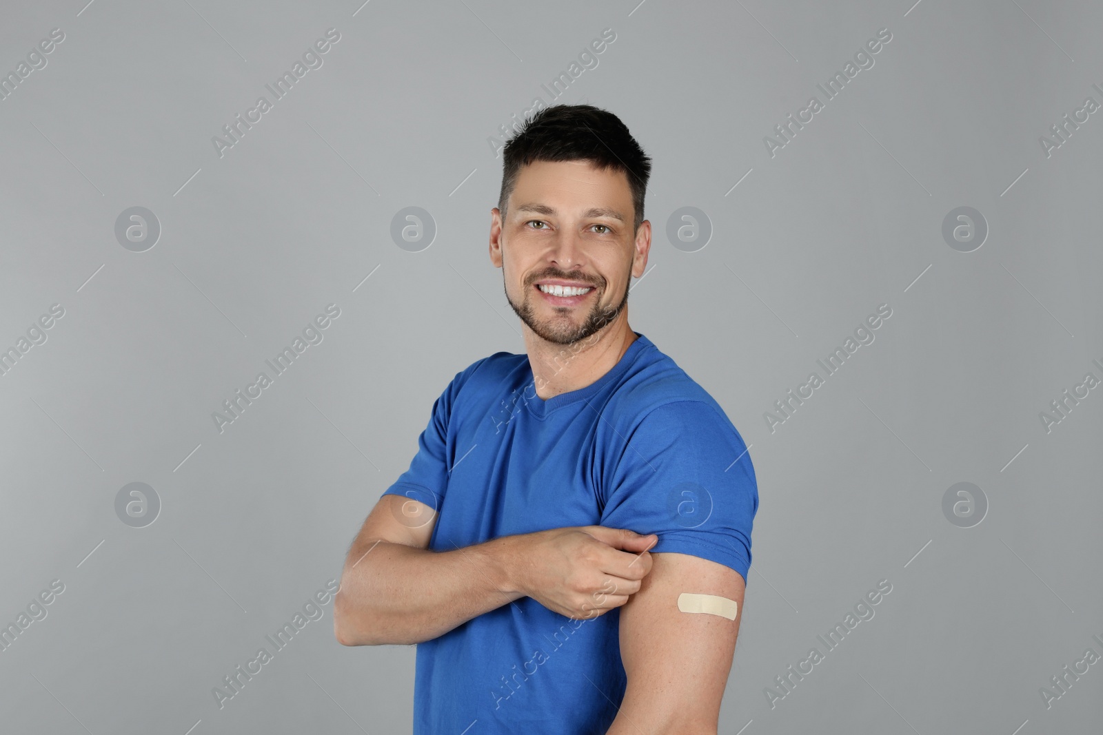 Vaccinated man with medical plaster on his arm against grey background Photo of Vaccinated man with medical plaster on his arm against grey background