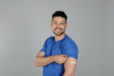 Vaccinated man with medical plaster on his arm against grey background Photo of Vaccinated man with medical plaster on his arm against grey background