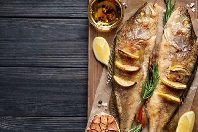 Photo of Tasty homemade roasted perches on black wooden table, top view and space for text. River fish